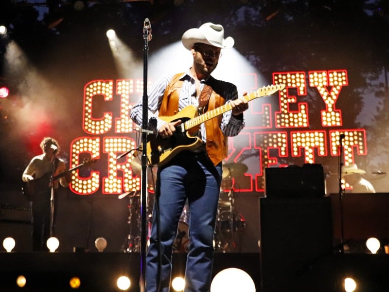 Charley Crockett stands with his guitar on stage.
