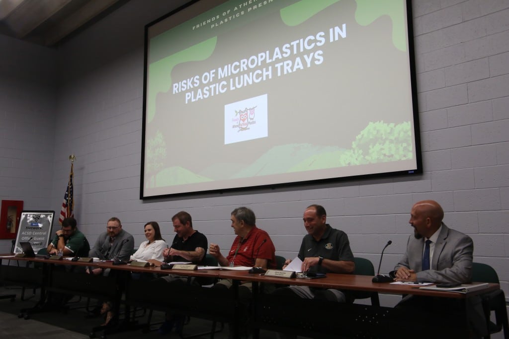 Group of people sitting at a table with a presentation on a screen behind them